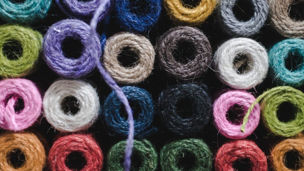 Rows of thread spools in many different colours, one strand pulled loose across them